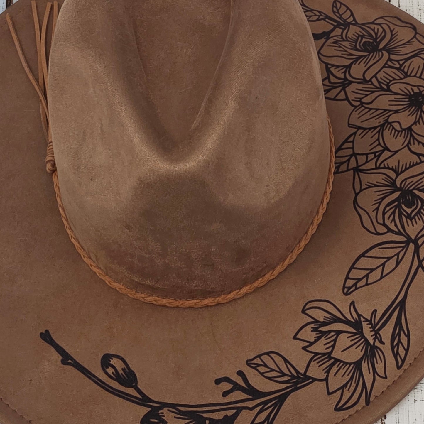 Elkhorn Designs chestnut vegan suede wide brim hat with intricate laser-engraved gardenia floral design and braided band.