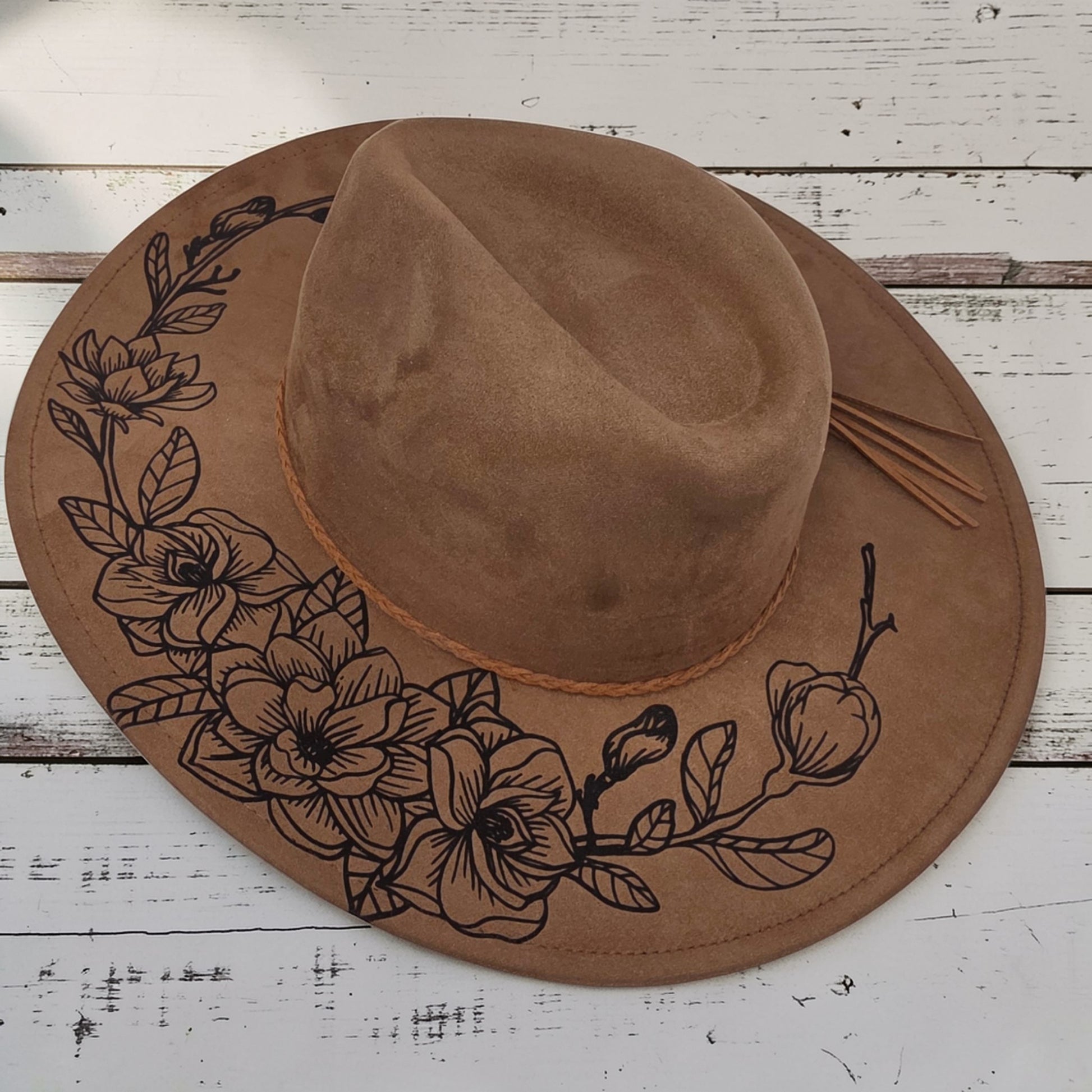 Elkhorn Designs chestnut vegan suede wide-brim hat with laser-engraved gardenia floral design and braided tassel band.
