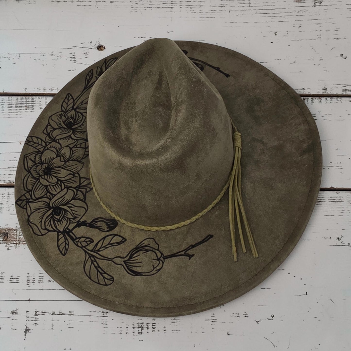 Elkhorn Designs sage green vegan suede wide-brim hat with laser-engraved gardenia floral details and braided band.