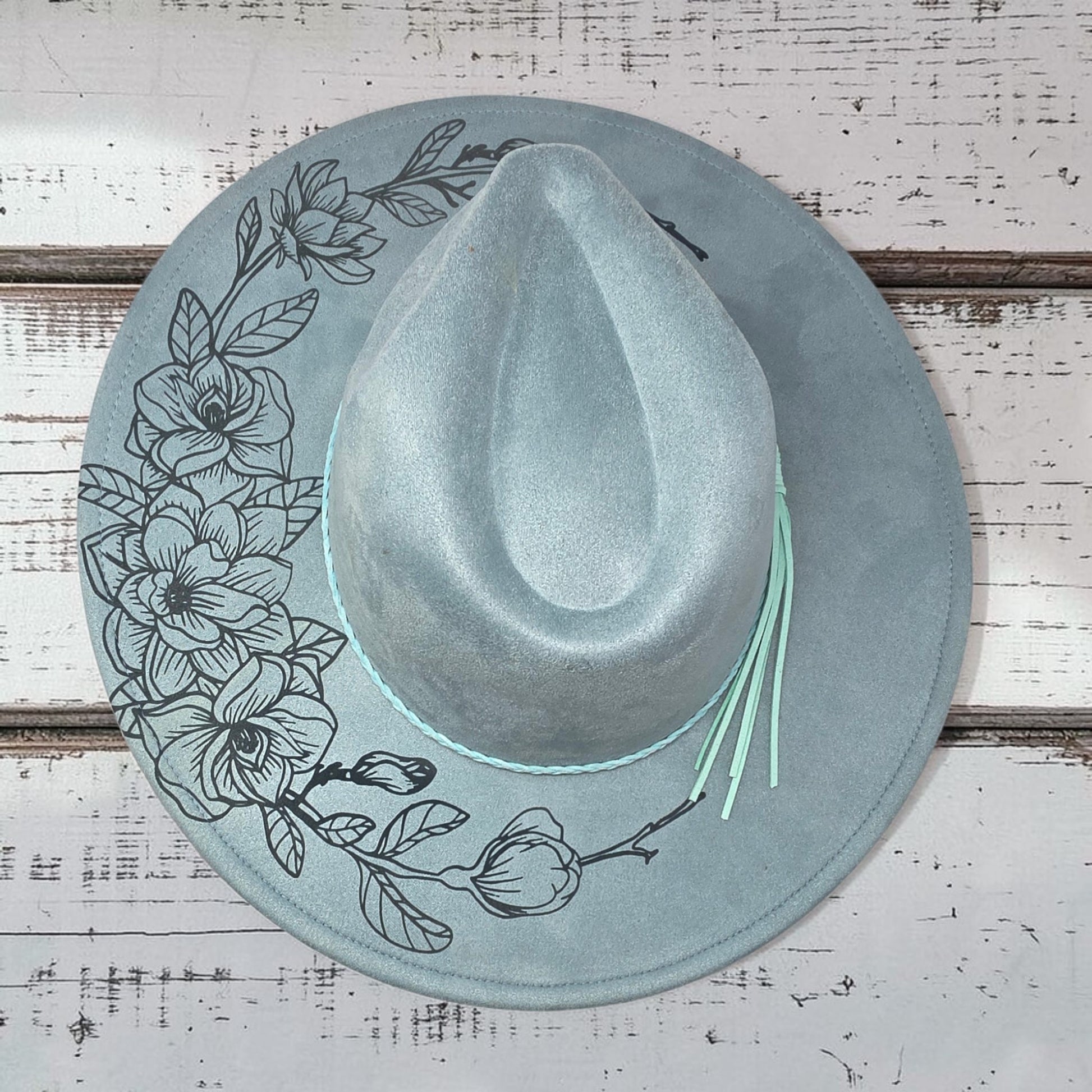 Elkhorn Designs sea glass green vegan suede wide brim hat with laser-engraved gardenia floral design and tassel band