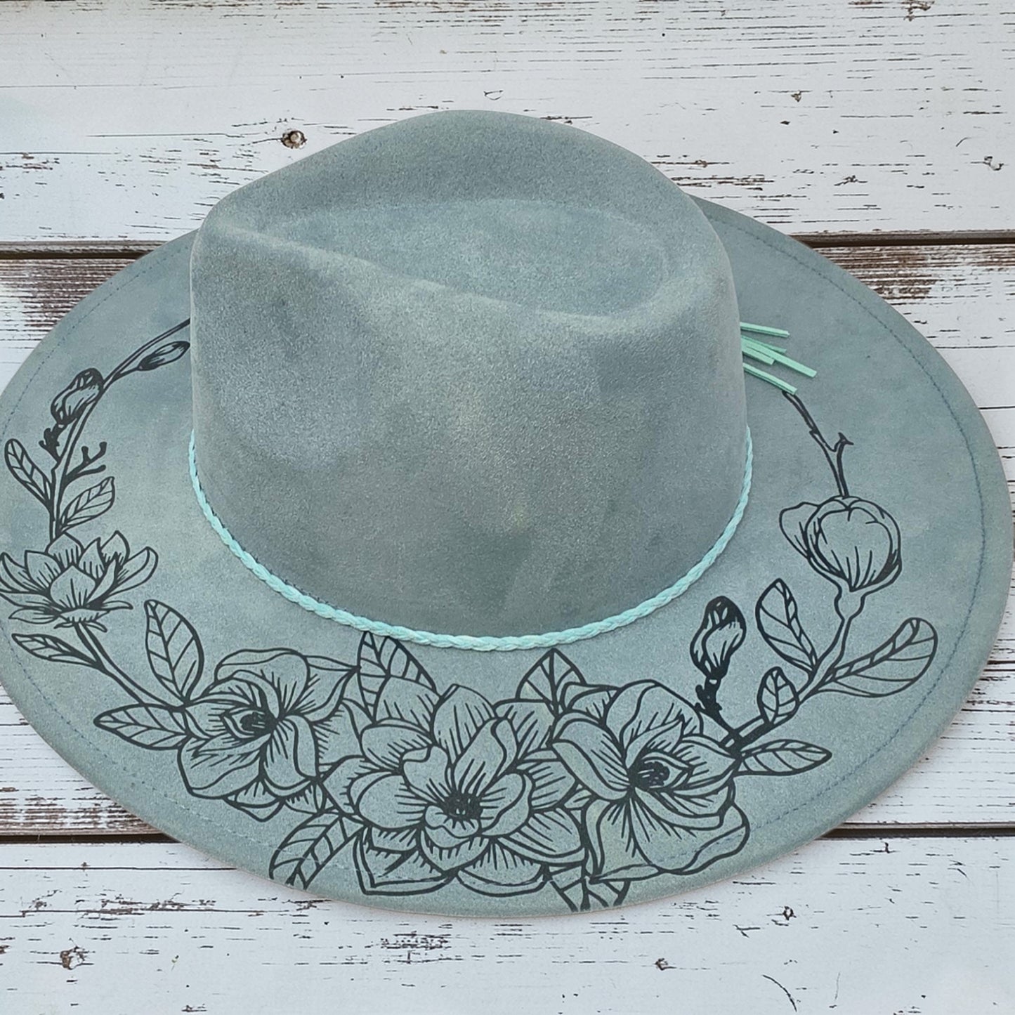 Elkhorn Designs sea glass green vegan suede wide brim hat with laser-engraved black gardenia floral design
