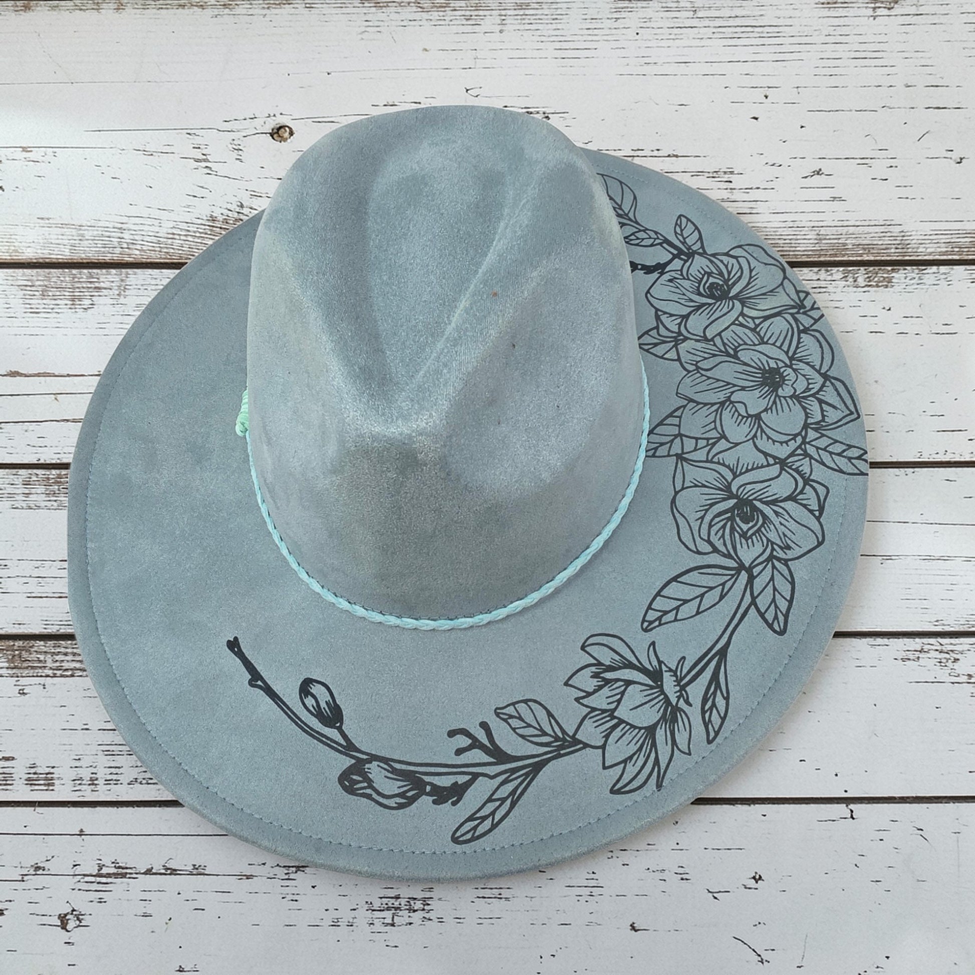 Elkhorn Designs sea glass green vegan suede wide brim hat with laser-engraved gardenia floral design and braided band