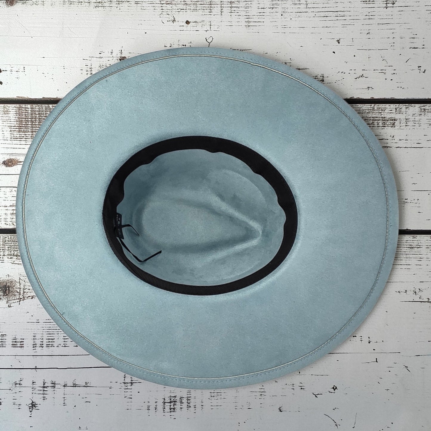 Elkhorn Designs sea glass green vegan suede wide brim hat with laser engraved floral details on a white wood surface